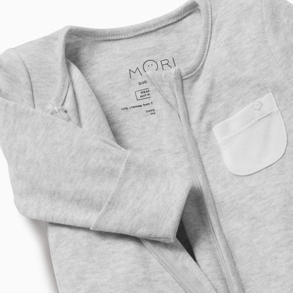 Close-up of the MORI Clever Zip Sleepsuit in grey, showcasing the two-way front zip, long sleeves, and a small white chest pocket for added detail.