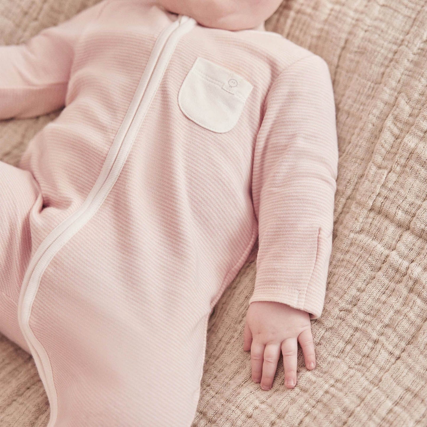 Baby wearing the MORI Clever Zip Sleepsuit in blush stripe, featuring a front zip closure and a small white pocket, designed for comfort and easy changing