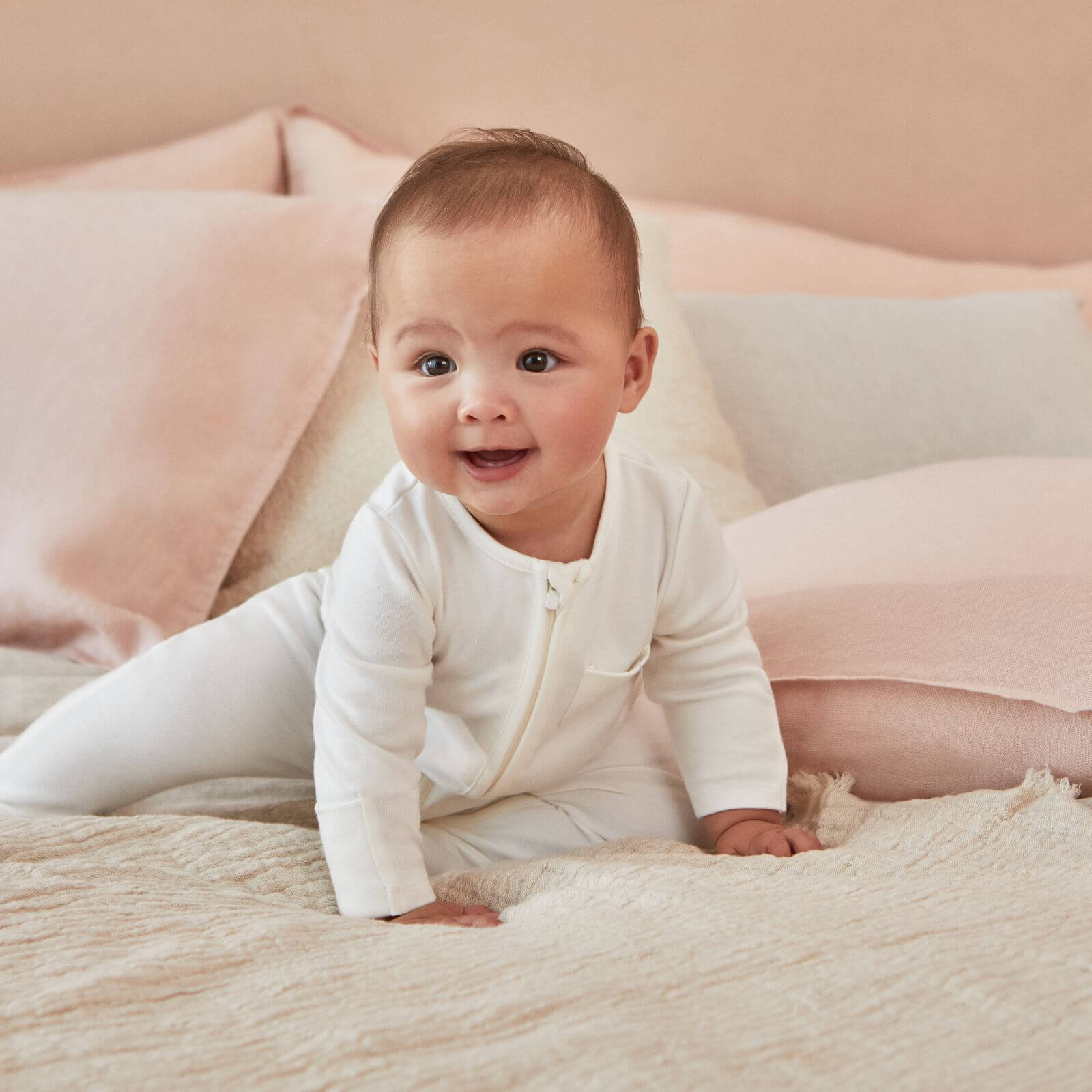 Baby crawling on a bed wearing the MORI Clever Zip Sleepsuit in white, featuring a two-way zip and a small chest pocket, designed for comfort and easy changing