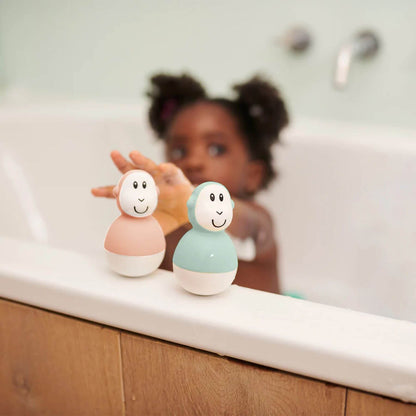 A child in a bathtub reaches for two Matchstick Monkey wobblers on the tub’s edge, with light wooden panelling in the background.