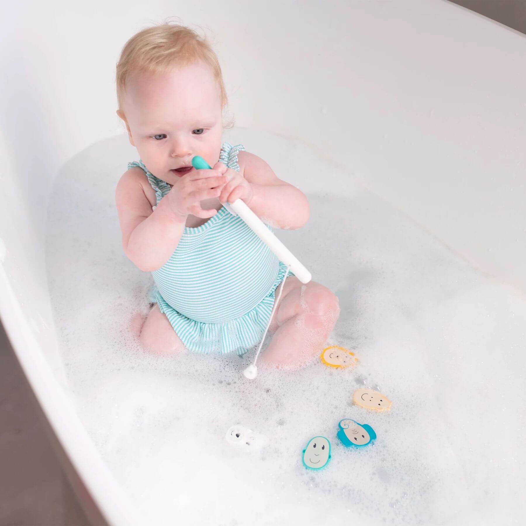 A baby plays in a bubble bath with the Matchstick Monkey fishing game, designed to develop hand-eye coordination and motor skills for 12 months+.