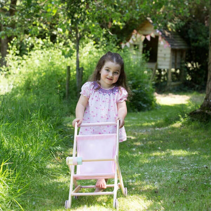 Child pushing a Moover Toys pink wooden dolls' stroller with pastel beads, enjoying outdoor play and building motor skills.