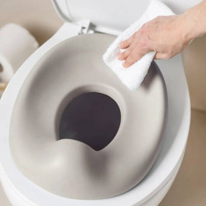 A  hand wiping the Nattou potty seat, highlighting its smooth, easy-to-clean surface.