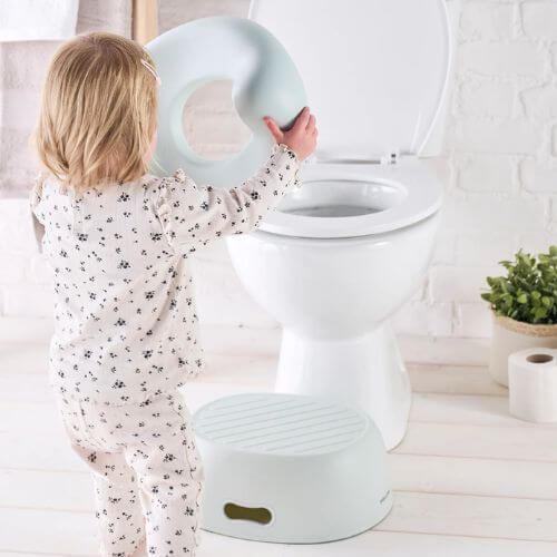 Toddler placing the Nattou green 3-in-1 potty seat on the toilet, learning to transition from the potty to using the toilet independently.