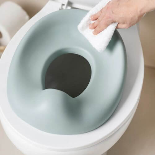 A hand wiping a green potty seat on a toilet, highlighting its easy-to-clean, hygienic surface.