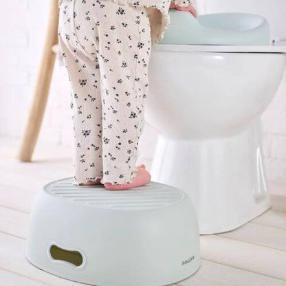 Child standing on a green step stool to reach the toilet, demonstrating how it supports independent toilet training.