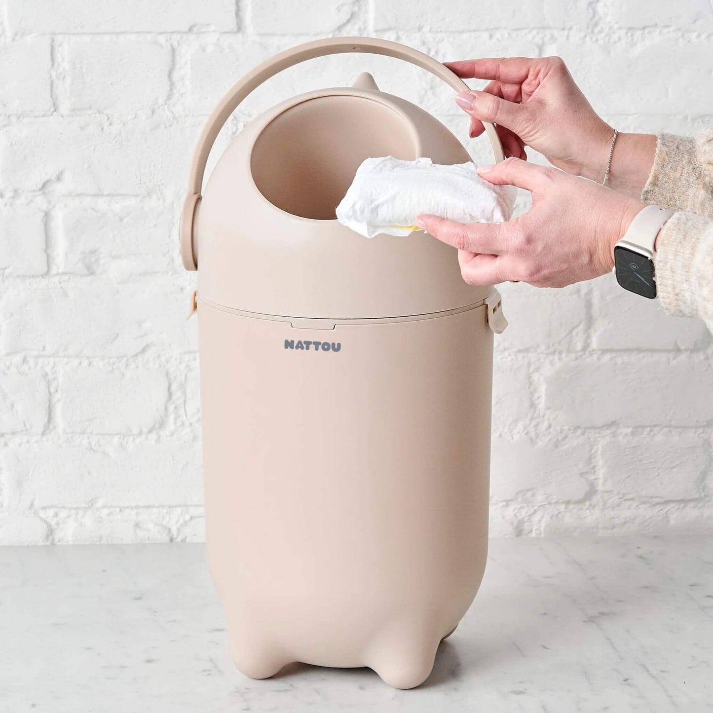 A hand holding a nappy over the open Nattou Dropy Nappy Bin, demonstrating its easy one-hand operation.