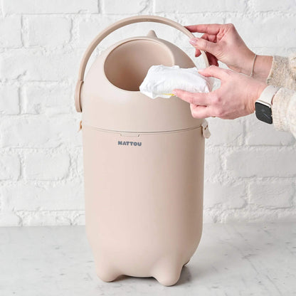 A hand holding a nappy over the open Nattou Dropy Nappy Bin, demonstrating its easy one-hand operation.