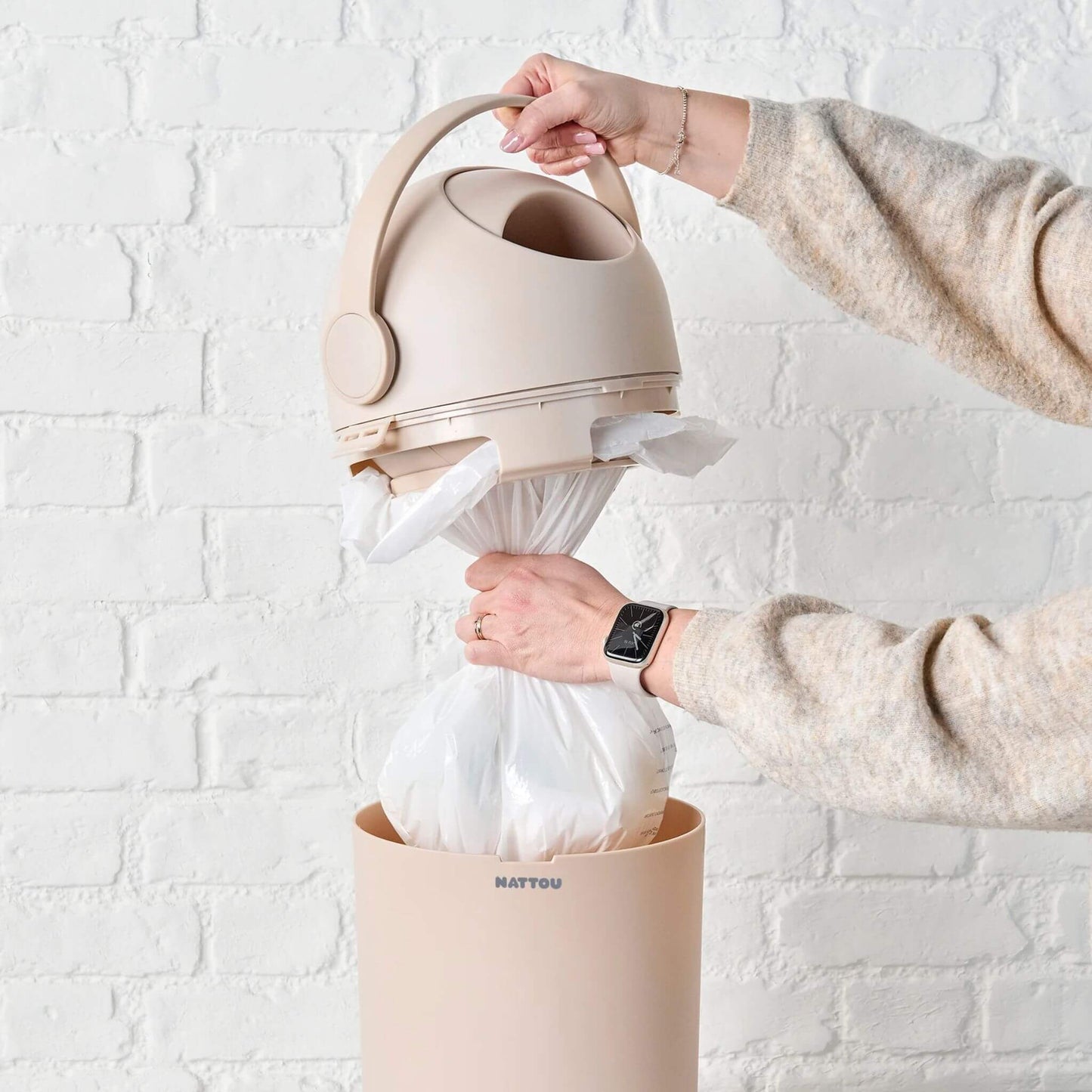 A person removing a full plastic bag from the Nattou Dropy Nappy Bin, highlighting its compatibility with standard bags.