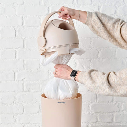 A person removing a full plastic bag from the Nattou Dropy Nappy Bin, highlighting its compatibility with standard bags.