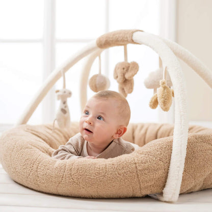 Smiling baby lying on their tummy in the Nattou Teddy Playmat, gazing up at soft hanging toys, including an elephant and giraffe.