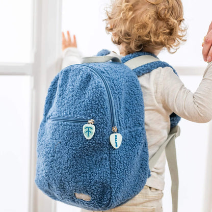 Toddler wearing the blue Nattou Teddy Backpack, holding a parent's hand while looking out a window.