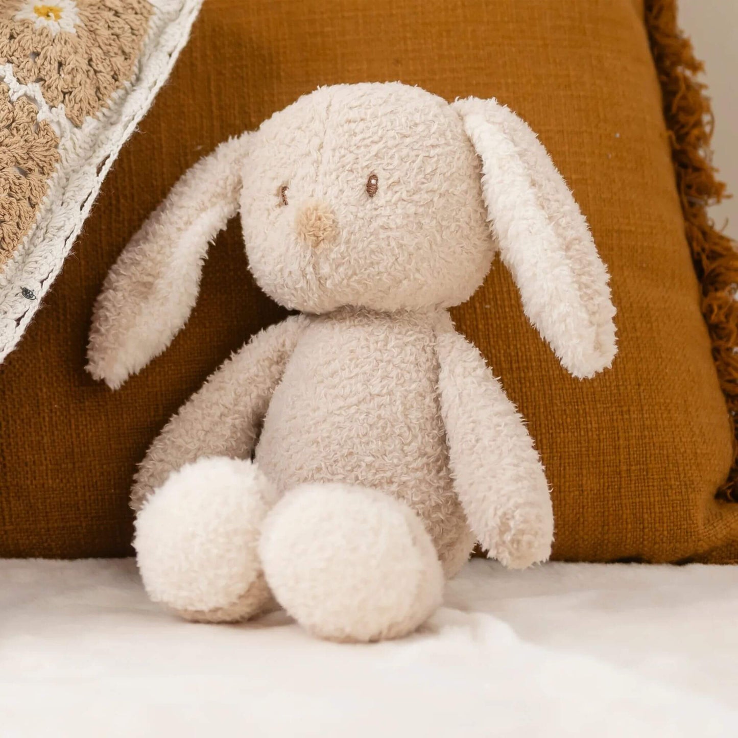 Nattou Bunny Teddy Cuddly resting on a cosy bed with warm-toned cushions, creating a soft and comforting nursery feel.