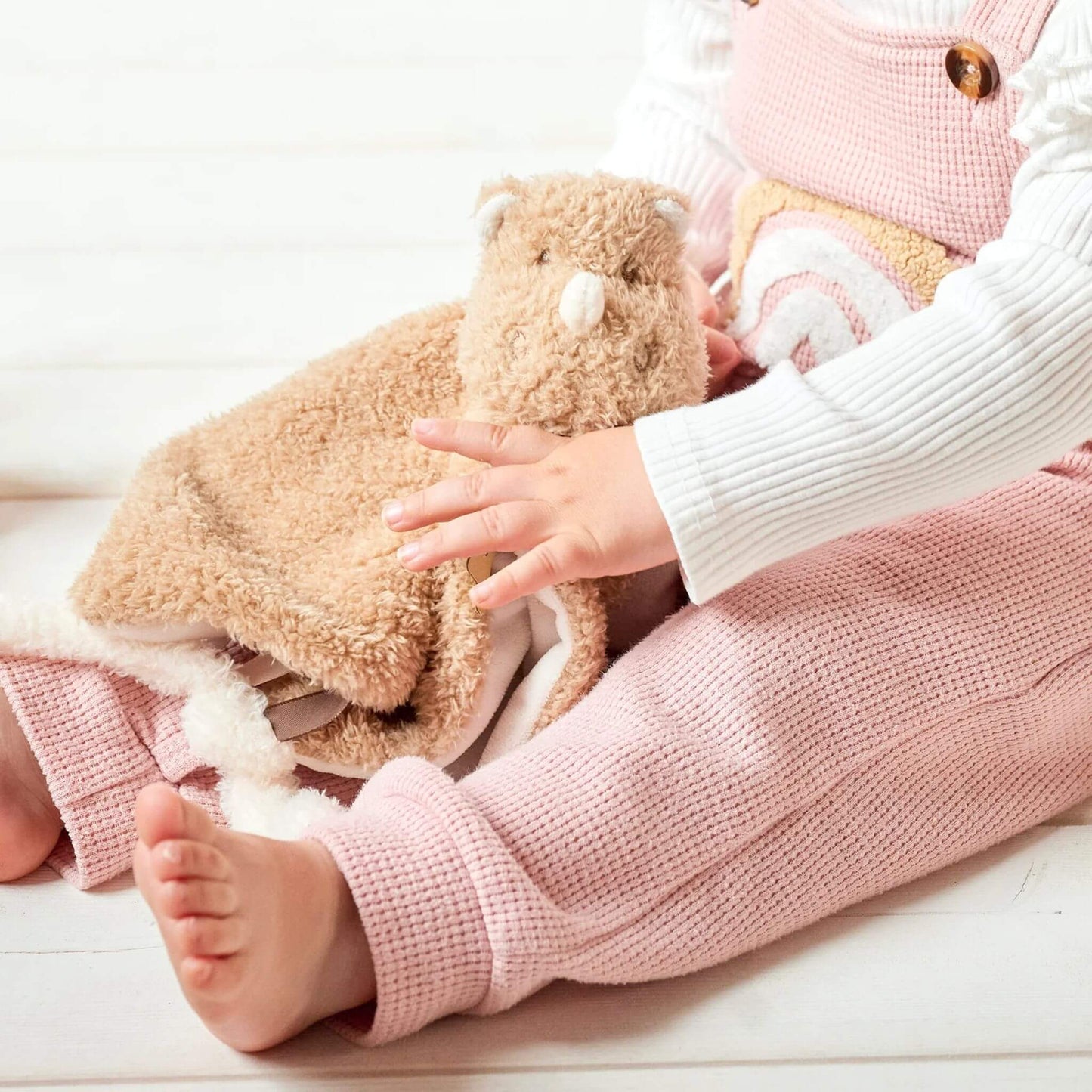 Baby's hands holding Nattou Teddy Rhino Doudou, showing soft tan material and sensory ribbon details.