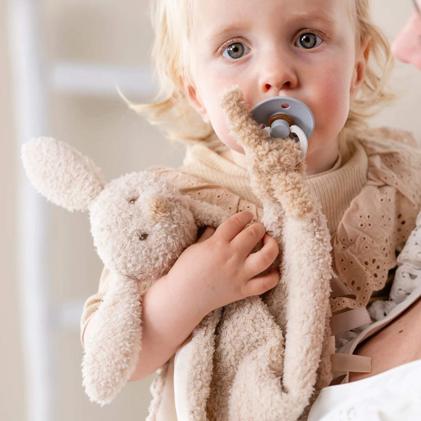 Toddler holding Nattou Bunny Teddy Maxi Doudou comfort blanket, showcasing soft beige plush material and comforting design.