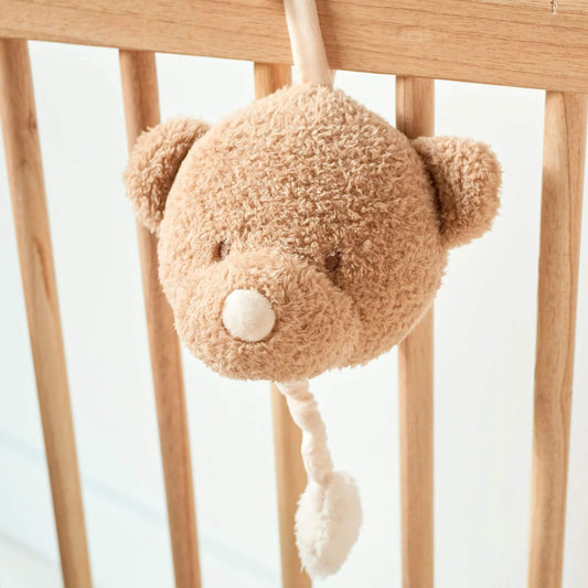 Nattou Teddy Musical Bear attached to wooden crib, with soft beige plush face and white pull cord for gentle bedtime melodies