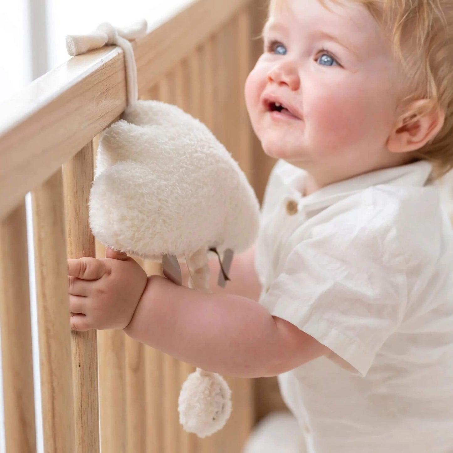 Smiling baby in a cot holding the Nattou Teddy Musical Cuddly, enjoying its soft texture and calming music.