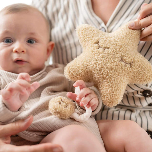 Baby holding the Nattou teddy star musical cuddly while seated, gently pulling the music cord.