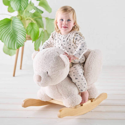 Smiling toddler riding the Nattou Teddy Bear Rocker in ecru. Set in a bright, cosy room with soft textures and natural wood accents.