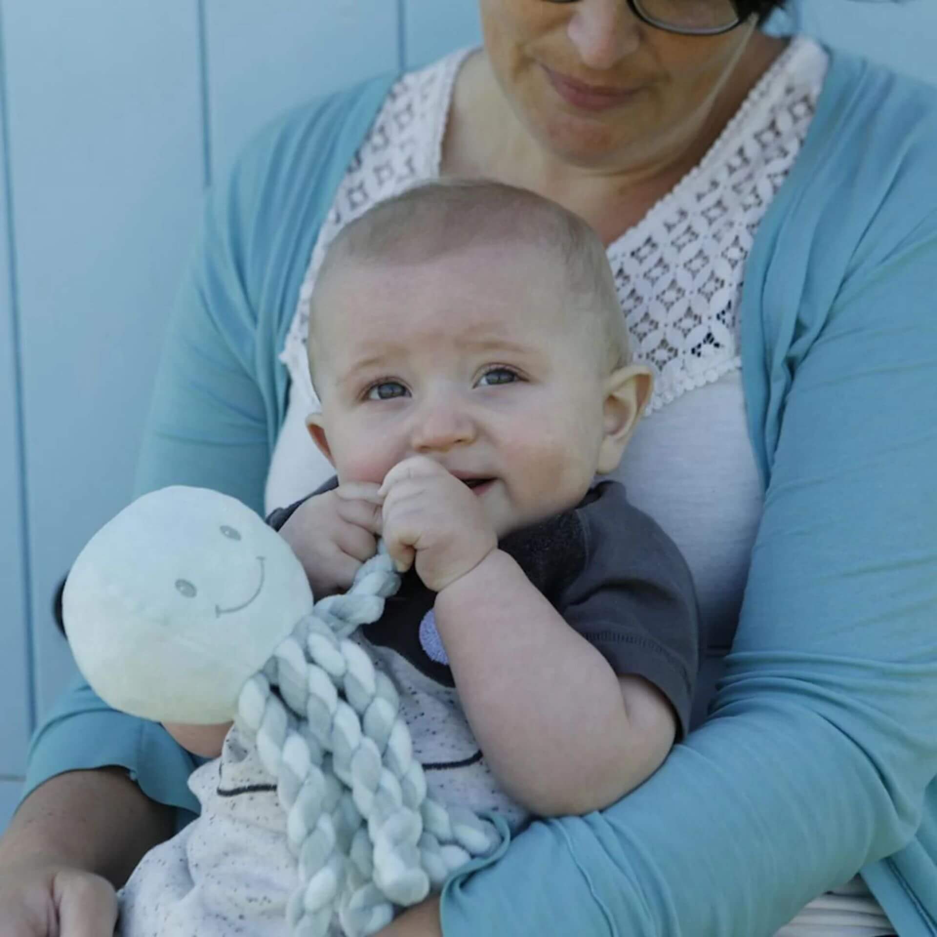 A baby chews on the mint green Nattou Piu Piu octopus with soft, twisted tentacles while being held, offering comfort and sensory stimulation.