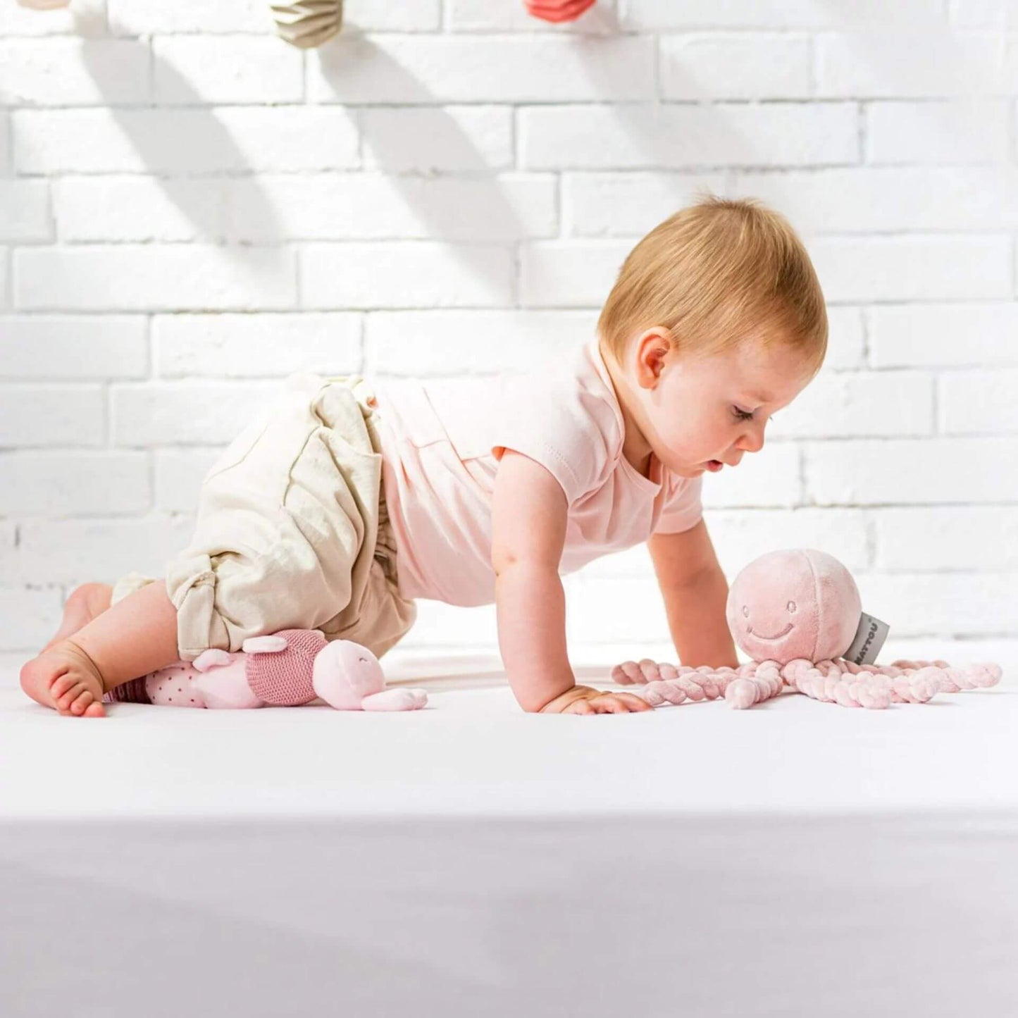 A baby crawls towards the pink Nattou Piu Piu octopus, featuring soft twisted tentacles, ideal for sensory play and comforting newborns.