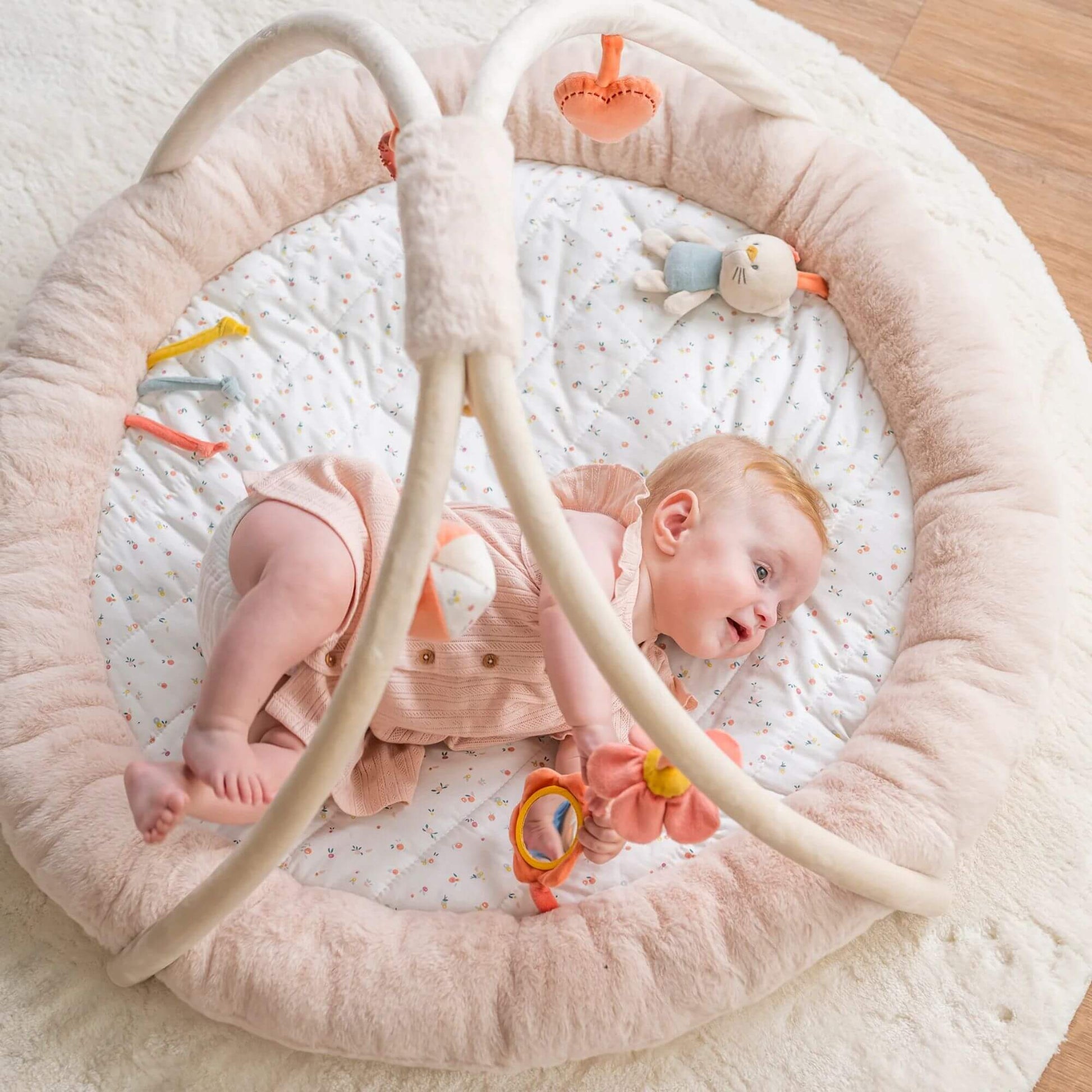 Baby lying on a Nattou Mila, Lana & Zoe stuffed playmat, featuring soft, padded beige sides and a delicate floral-patterned mat for a soothing look.