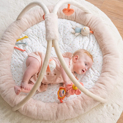 Baby lying on a Nattou Mila, Lana & Zoe stuffed playmat, featuring soft, padded beige sides and a delicate floral-patterned mat for a soothing look.