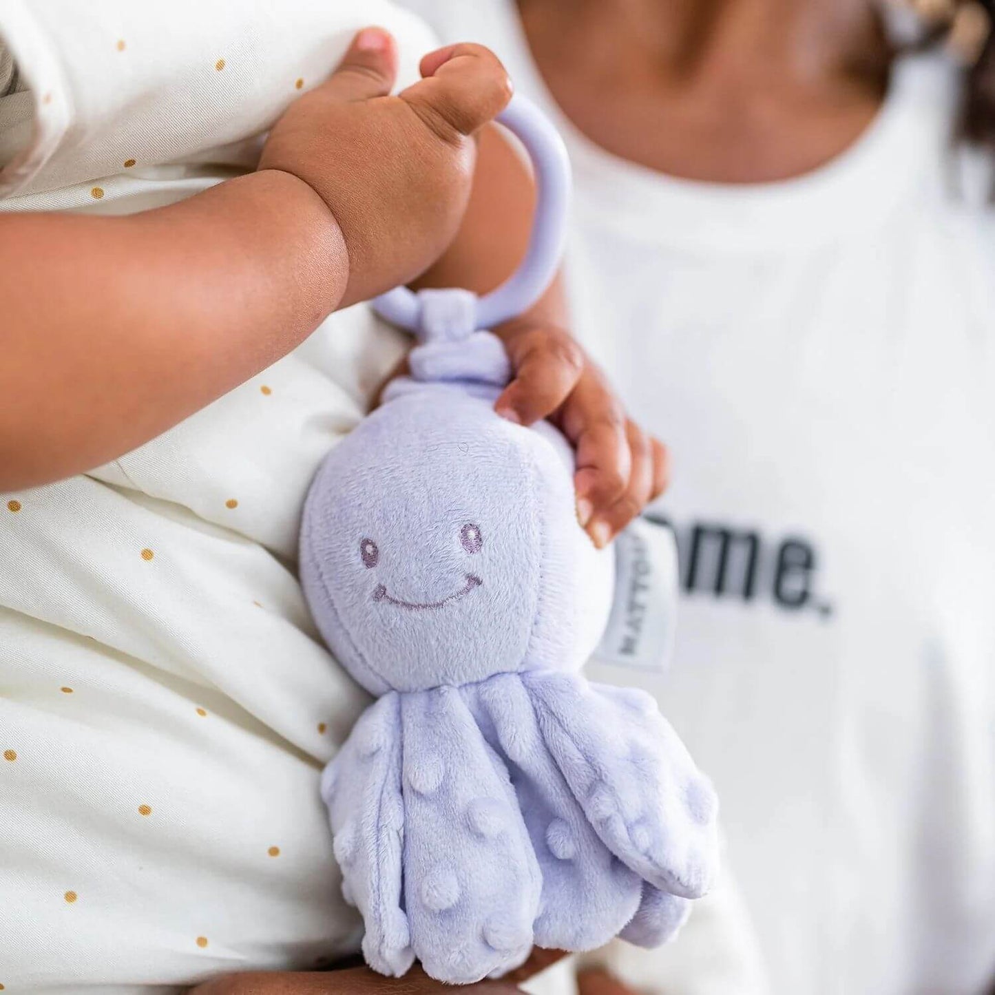 A baby holding the lilac Nattou Vibrating Octopus by its loop, while being carried by an adult.