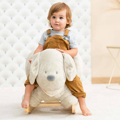 Toddler sits on Nattou Charlie the Dog rocker in vanilla, enjoying a cosy ride with a soft plush design and sturdy wooden base.