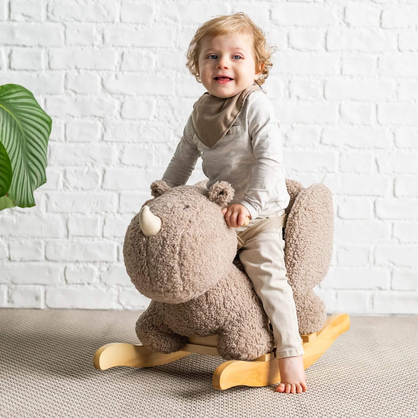 Smiling toddler sits on a plush Nattou rhino rocker with a sturdy wooden base, enjoying a safe and cosy rocking experience.