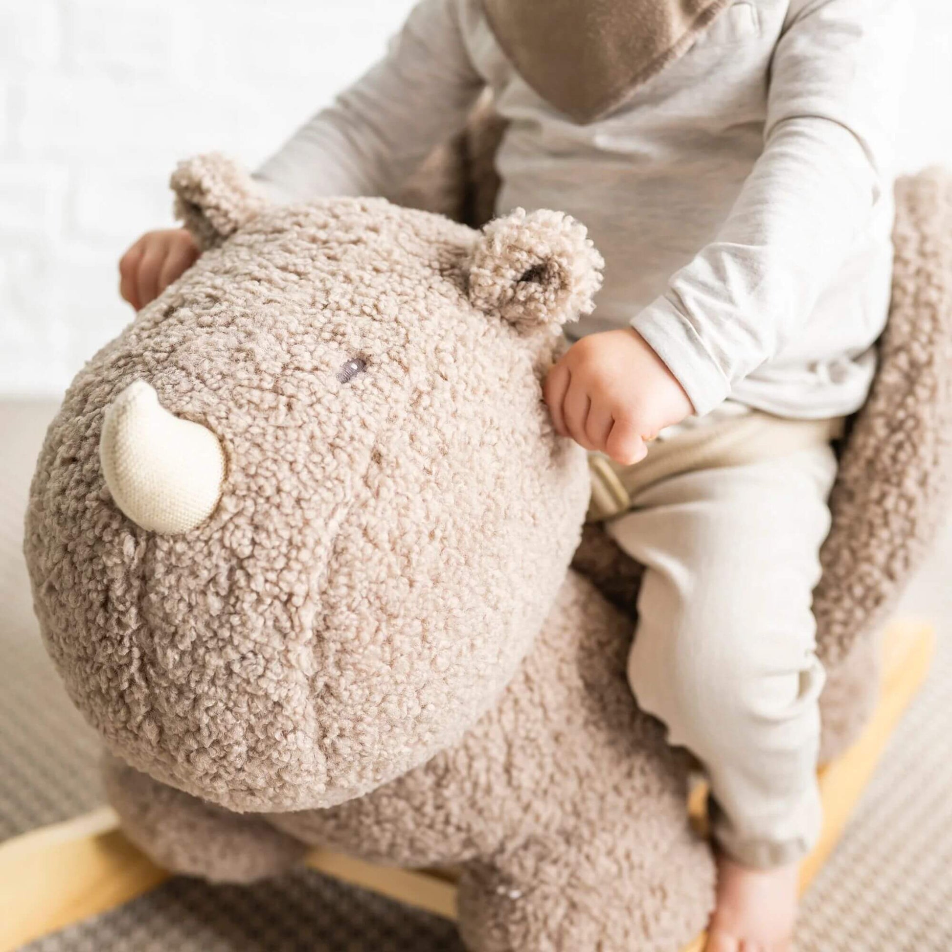 Close-up of toddler's hands holding onto a soft, plush Nattou rhino rocker, highlighting the cosy fabric and secure design.