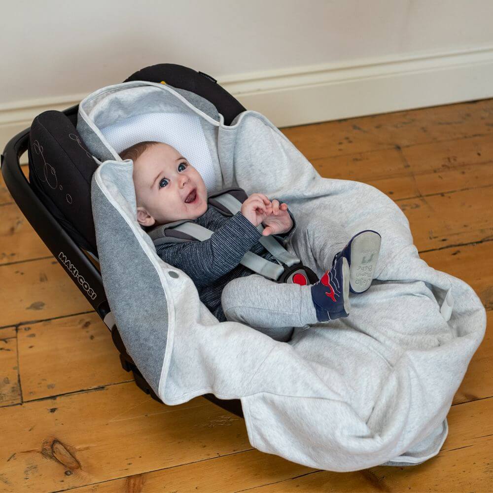 Baby sitting comfortably in a car seat with the Purflo Cosy Wrap in Minimal Grey, providing warmth and security with soft fabric.