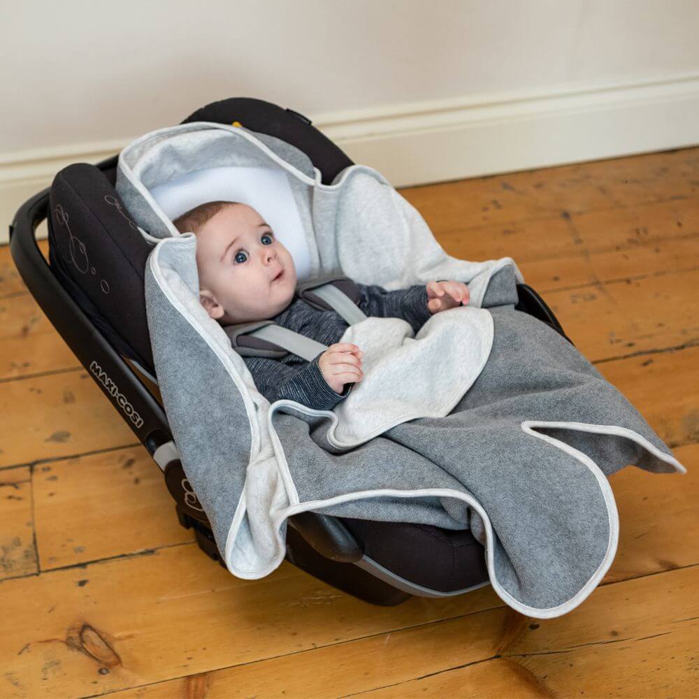 Baby snugly wrapped in the Purflo Cosy Wrap – minimal grey, buckled safely in a car seat. This soft wrap provides warmth and comfort.