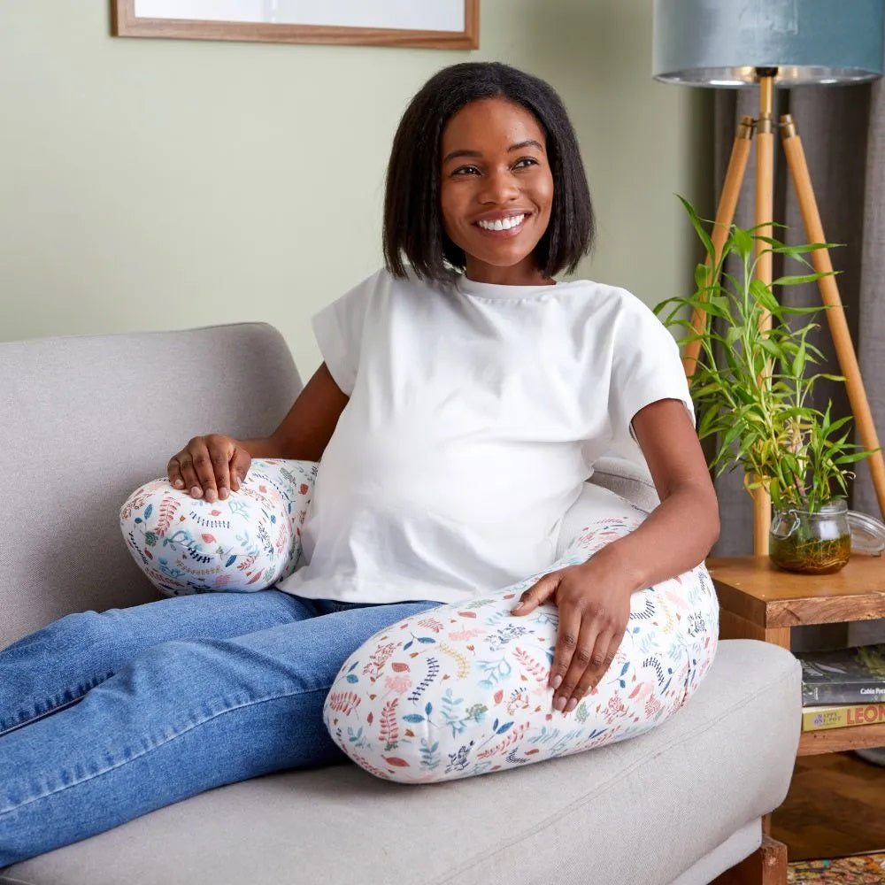 Pregnant woman relaxing on a sofa with the Purflo Breathe Pregnancy Pillow in Botanical print, providing ergonomic support and comfort.