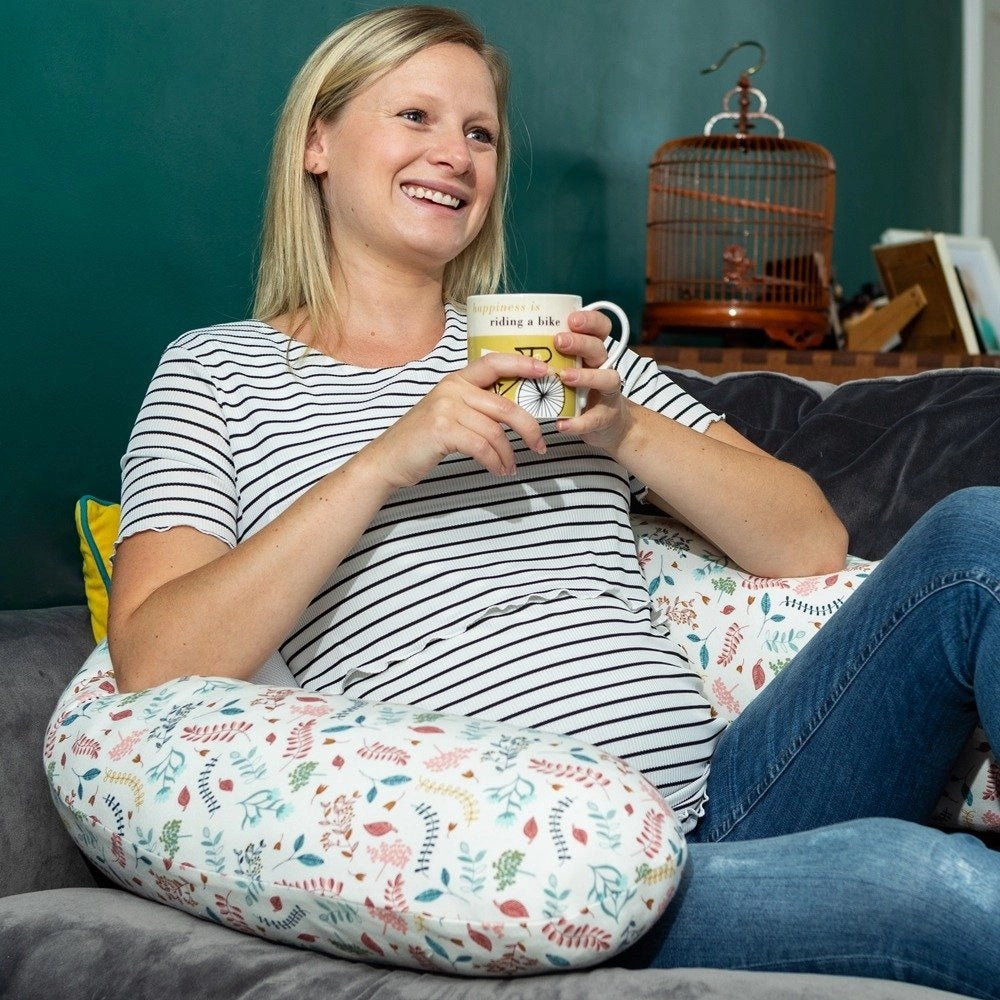 Pregnant woman relaxing with a cup of tea, using the Purflo Breathe Pregnancy Pillow in Botanical print for comfortable and supportive seating