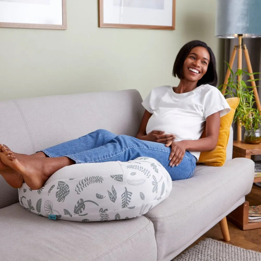 Woman relaxing on a sofa, using the Purflo Breathe Pregnancy Pillow in Botanical print for ergonomic leg support and comfort.