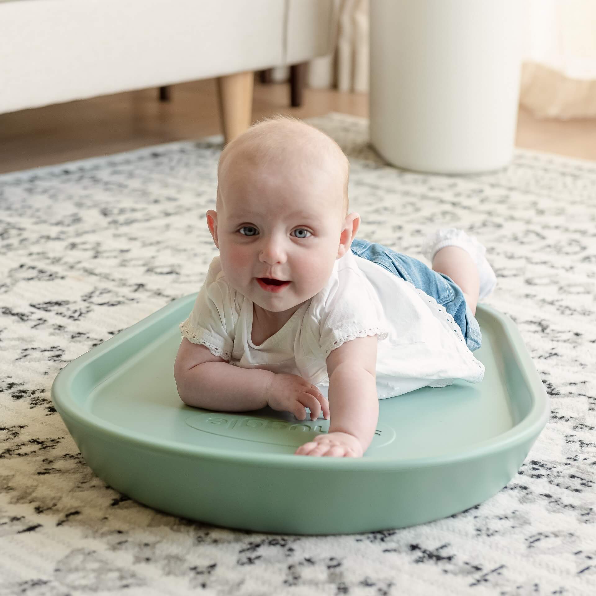 Happy baby in white top and denim lying on the eucalytpus Shnuggle Squishy Change Mat during tummy time, showing versatile usage beyond nappy changes.