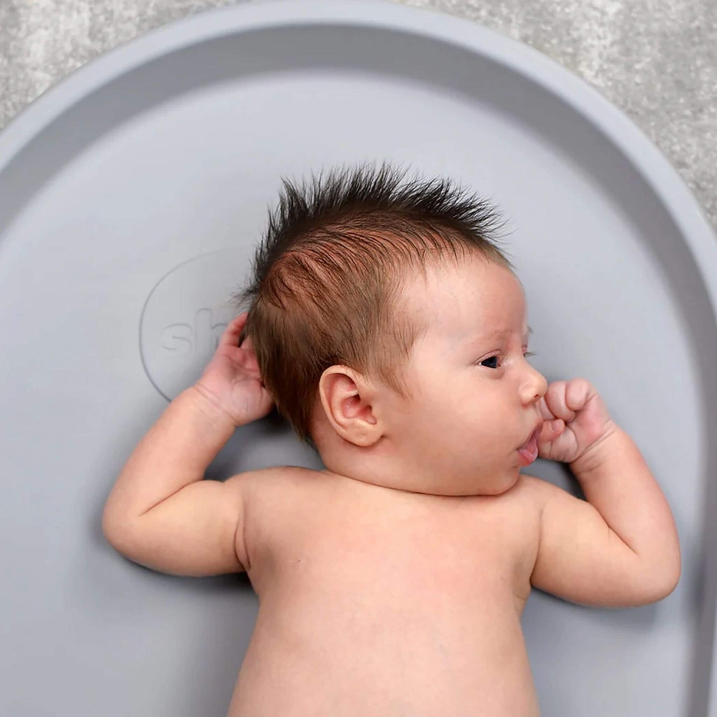 Newborn baby lying comfortably on the Shnuggle Squishy Changing Mat in grey, showing soft support for nappy changes.