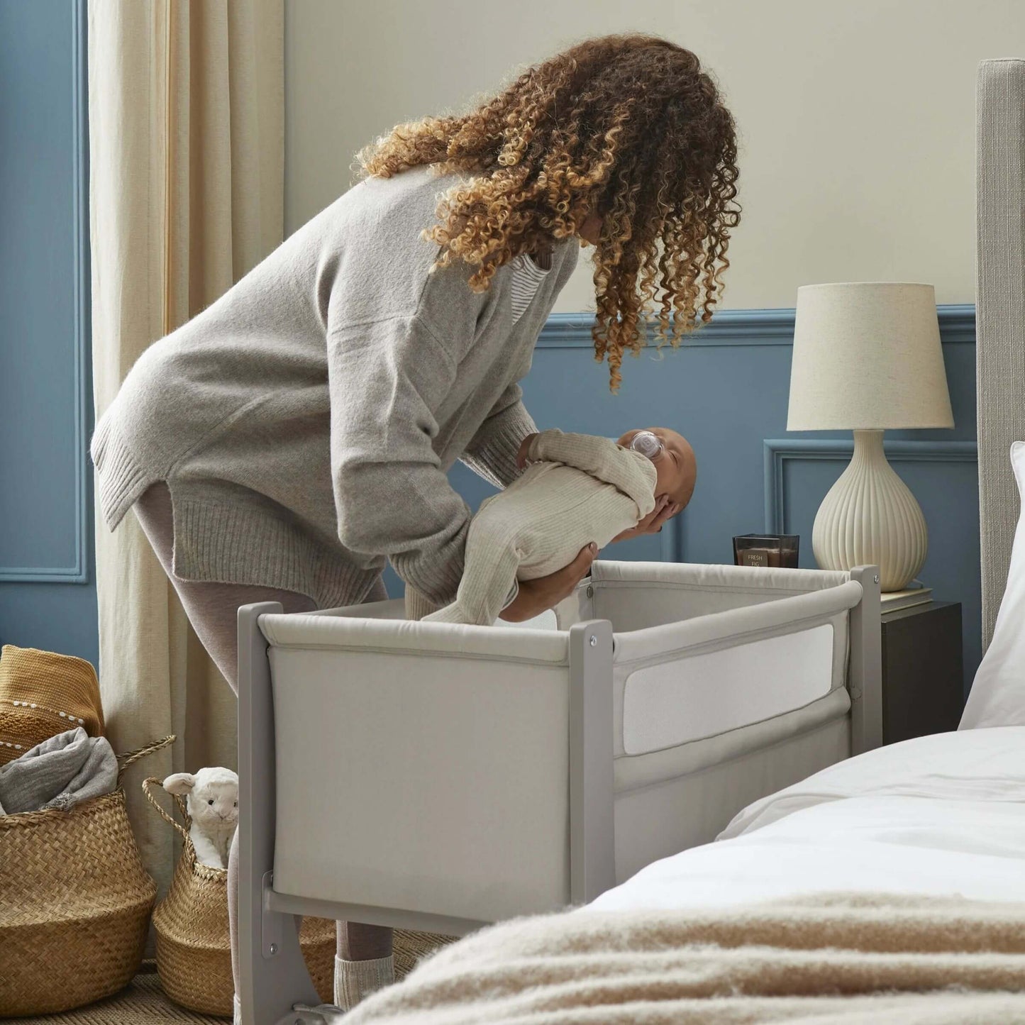 Mother gently placing baby into Shnuggle Air Lite Bedside Crib, illustrating ease of use and secure sleep environment.