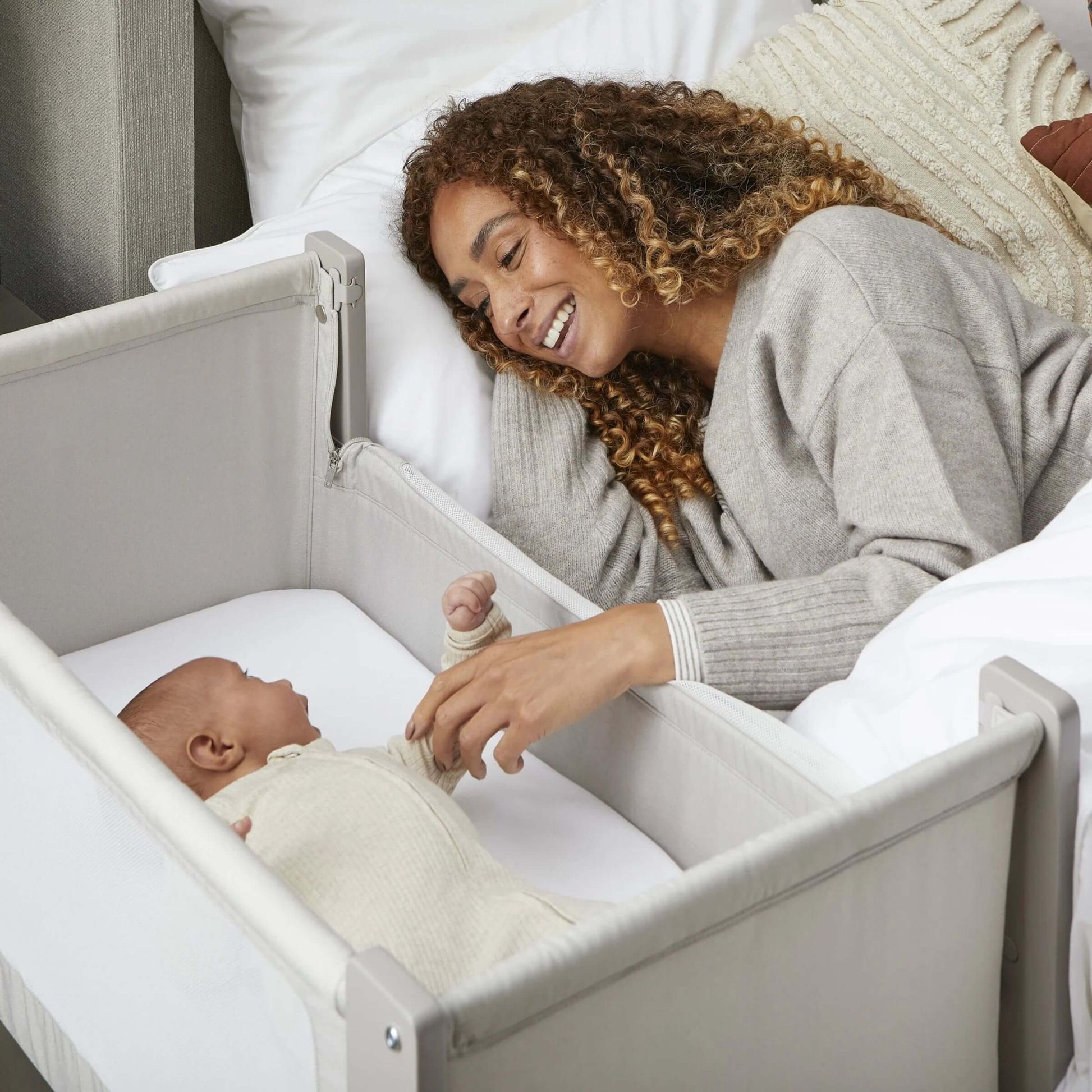 Mother smiling and reaching out to baby in Shnuggle Air Lite Bedside Crib, fostering bonding.