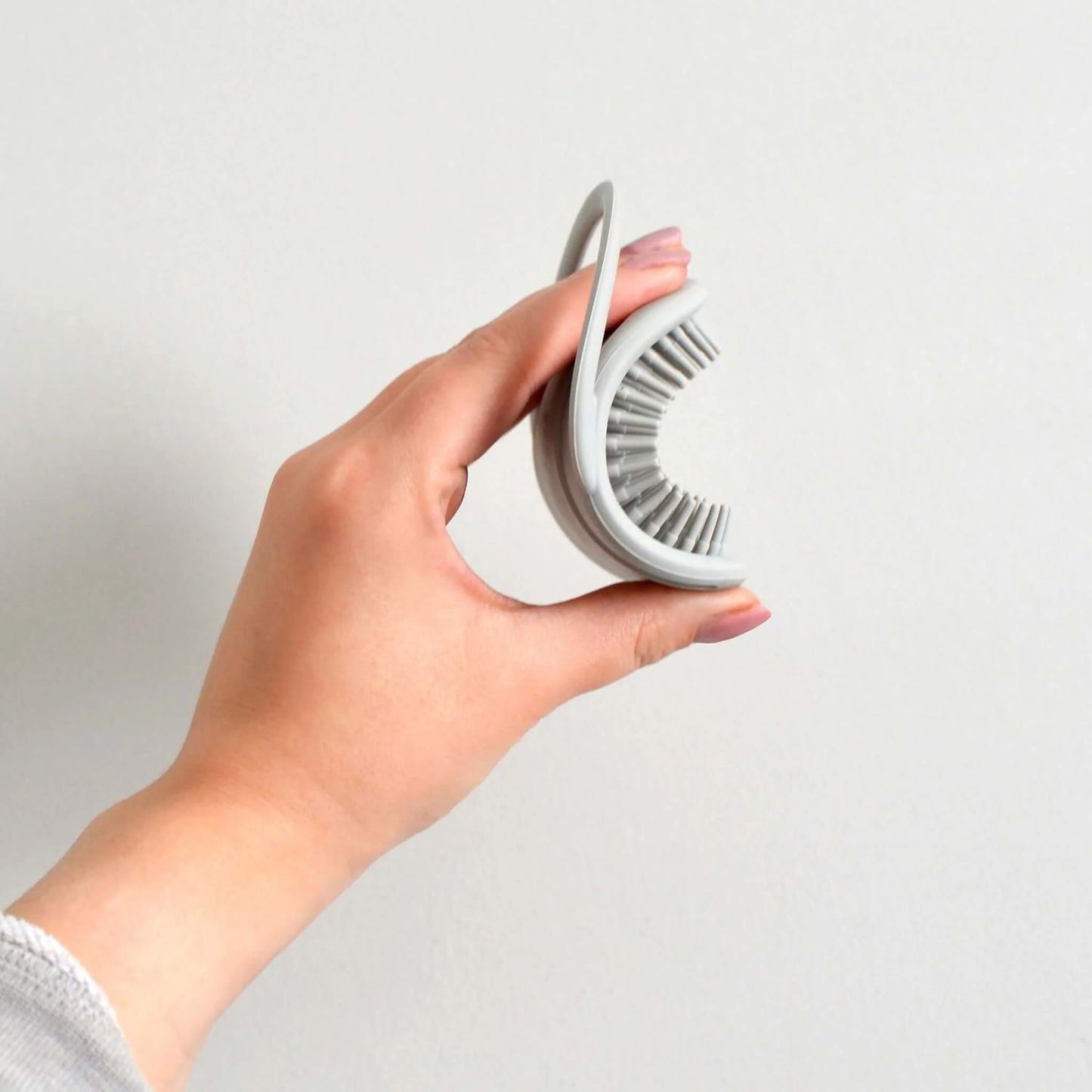 Side view of a hand holding the flexible Shnuggle baby bath brush in grey, showing the soft silicone bristles and bendable design.