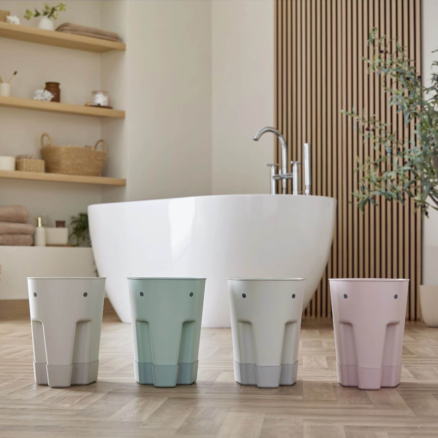 Four Shnuggle bath toy drying caddies in various colours lined up in a modern bathroom with a freestanding tub.