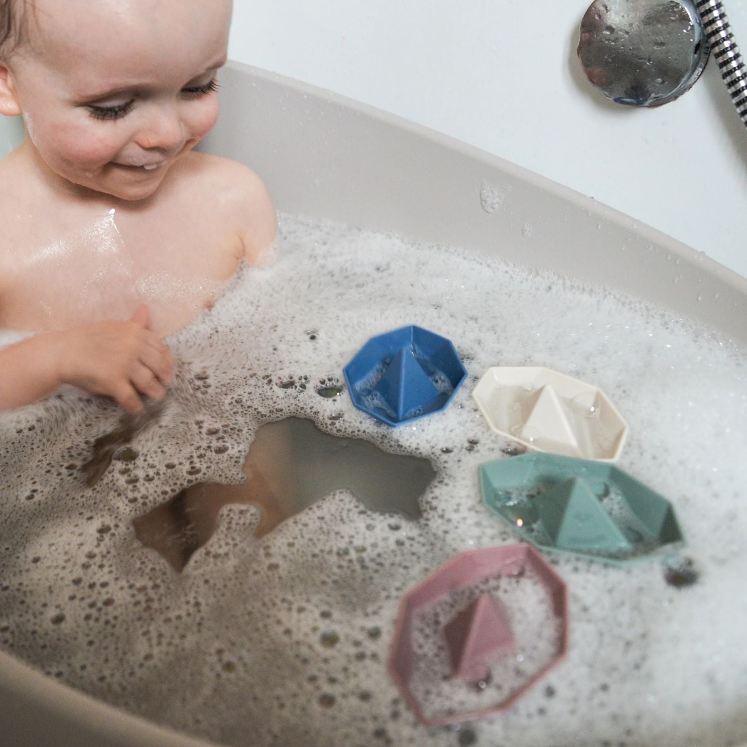 Smiling child playing in the bath with Shnuggle Stack ‘n’ Sail Bath Boat Toys, floating among bubbles.