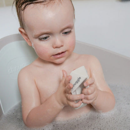 Child playing in the bath with a Shnuggle Stack ‘n’ Sail Bath Boat Toy, holding it in both hands and enjoying bath-time fun