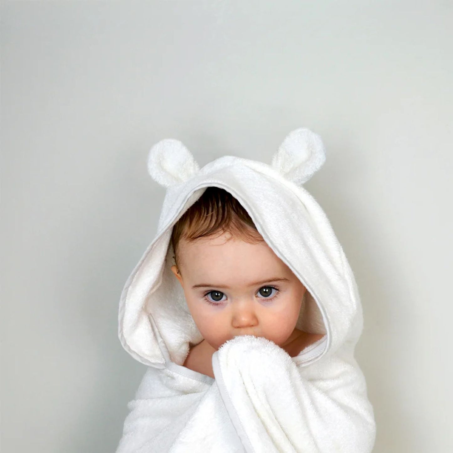 Baby snuggled in a Shnuggle wearable bath towel with hood featuring cute ears, bringing warmth and comfort after bath time.