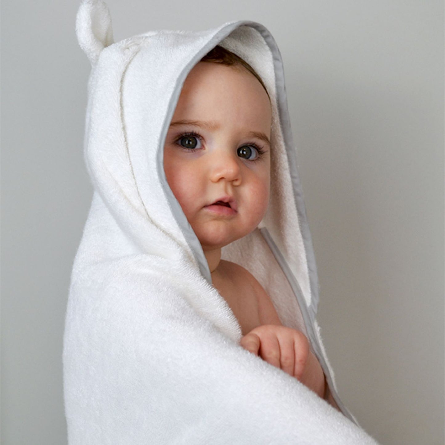 Baby wrapped snugly in a Shnuggle wearable bath towel with hood and cute ear detail, perfect for a cosy and dry post-bath cuddle.