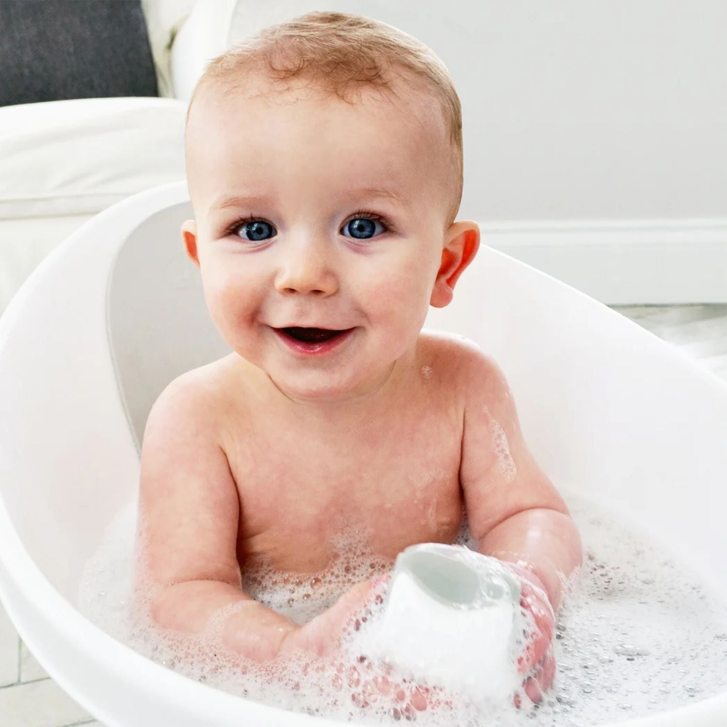 Smiling baby enjoying bath time with the Shnuggle Wishy Bath Toy, surrounded by bubbles in a Shnuggle bath tub.