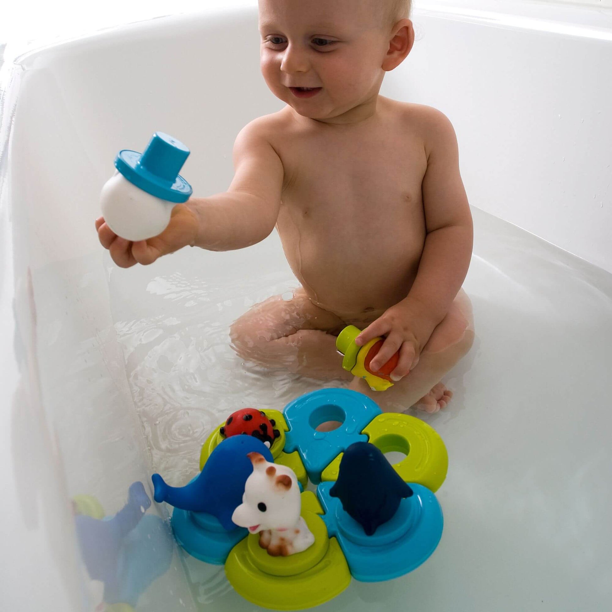 A baby enjoying bath time with the Sophie la Girafe Bath Puzzle, featuring floating animal figures and interactive puzzle pieces.