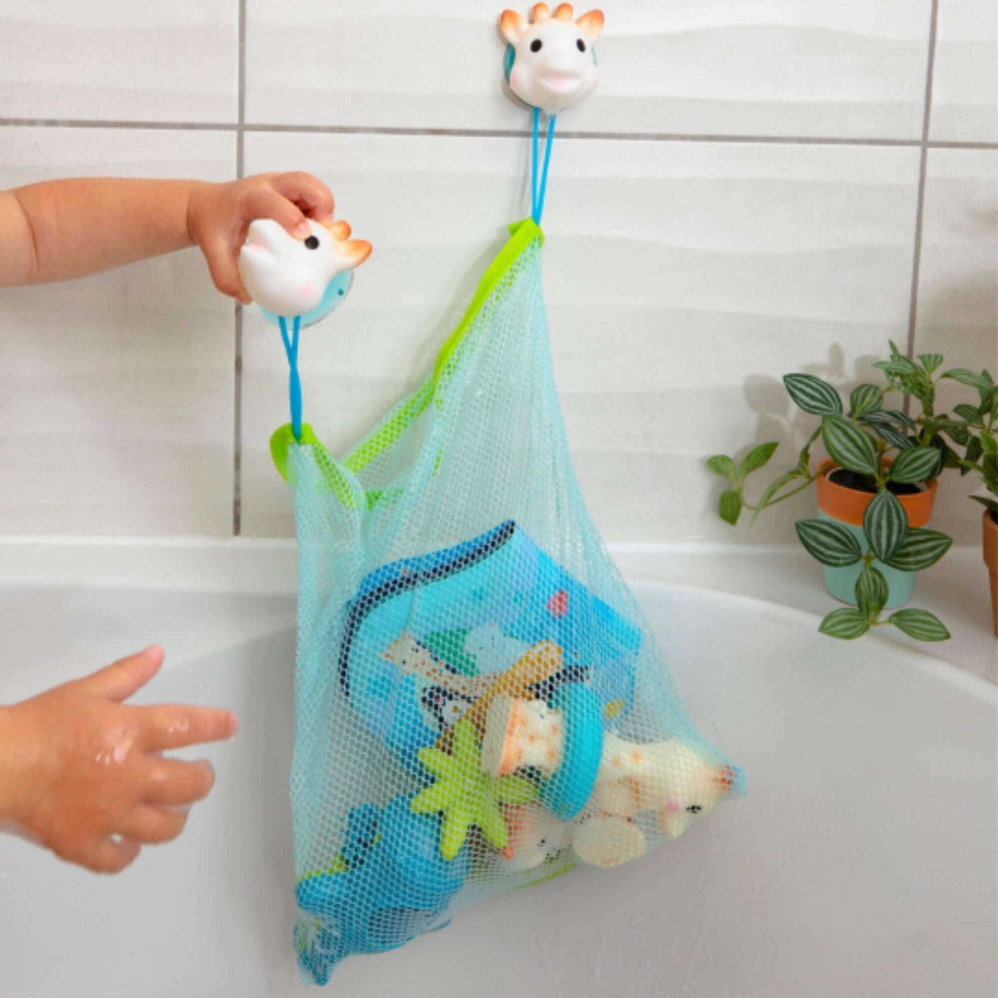 Sophie la Girafe bath toy storage net holding toys, attached to tiled walls with suction cups, keeping bath time tidy and organised.