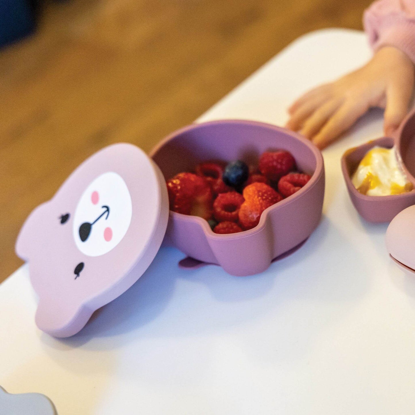 Pink TUM TUM bear-shaped snack pot filled with fresh berries, alongside a matching plate with yoghurt, perfect for toddlers learning to self-feed.